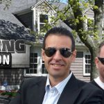 Two men in suits and sunglasses standing outside of a house.